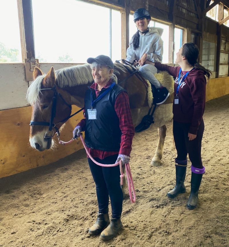 A rider in her lesson riding Lexie, supported by 3 volunteers. 
