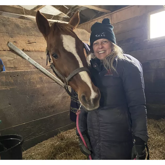 Deb smiling holding on to Lady's lead rope in her stall. Lady has her head curled around her with her ears forward.
